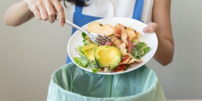 Žena sype do odpadkového koše zbytky zeleniny a ovoce.