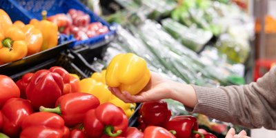 Ženská ruka vybírá papriku v supermarketu z regálu