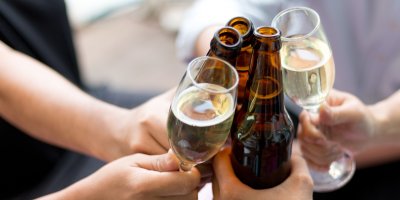 Tři lidé si přiťukávají lahví piva, dva skleničkami s bílým vínem