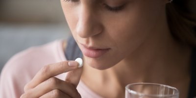 Žena si dává prášek, v druhé ruce drží sklenici s vodou