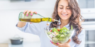 Žena zalévá mísu salátu olivovým olejem