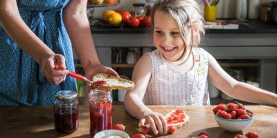 Žena maže dceři chléb jahodovou marmeládou
