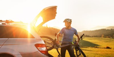 Muž nakládá cyklistické kolo do auta při západu slunce