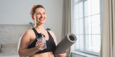 Žena ve sportovním oblečení drží podložku na cvičení a flašku