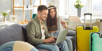 Mladý pár se dívá do notebooku a vedle má kufry