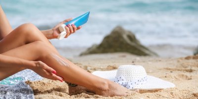 Žena si na pláži natírá nohy opalovacím krémem