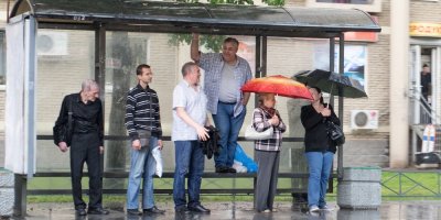 Skupina lidí schovávajících se před deštěm pod střechou autobusové zastávky