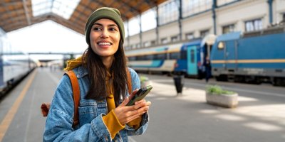 Žena stojí na vlakovém nádraží s mobilem v ruce