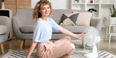 Žena sedí před přenosným větrákem na koberci v obýváku