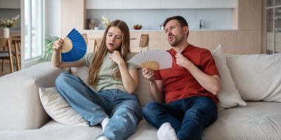 Muž a žena sedí na pohovce, ovívají se vějířem, protože je jim horko