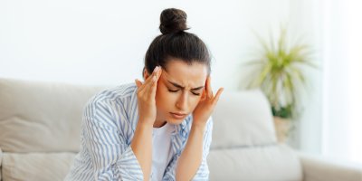 Žena sedí na gauči a drží se za hlavu