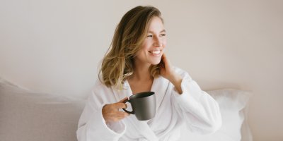 Mladá žena v županu drží hrnek a usmívá se