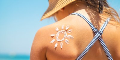 Žena v plavkách, která má na zádech opalovacím krémem nakreslené sluníčko