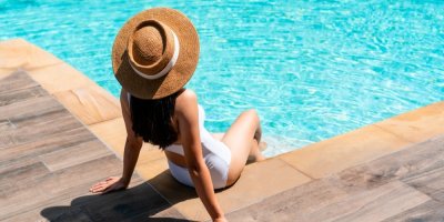 Žena v klobouku se opaluje u bazénu