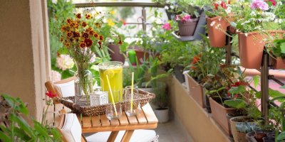 Balkon osázený truhlíky s květinami a posezením, na kterém je podnos s limonádou a dvěma skleničkami