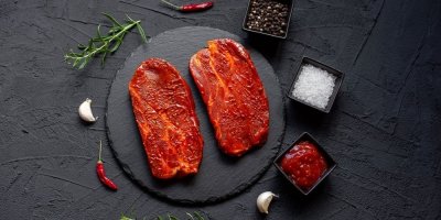 Dva marinované syrové vepřové steaky na kamenné podložce, koření a dochucovadla, pohled shora