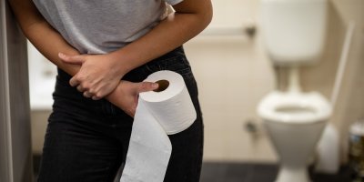 Žena se před toaletou drží za břicho a v ruce má toaletní papír