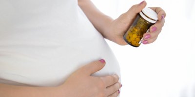 Těhotná žena drží v ruce lahvičku pilulek