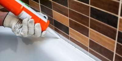 Člověk dává silikonový tmel do spáry kolem vany v koupelně 