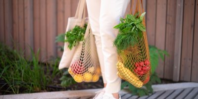 Žena drží nákup v síťovaných a látkových taškách.