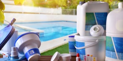 Různá technika k čištění bazénu: Bílo-modrý filtr, kbelíky a kanistry, bílé tablety položené na stolku