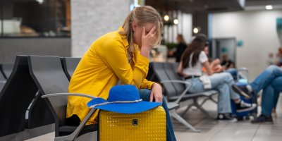 Žena sedí na letišti a má hlavu v dlaních