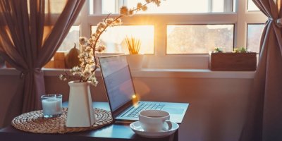 Notebook a šálek nápoje na stolku v místnosti, do které oknem svítí slunce