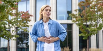 Žena stojí před budovou a drží se za břicho