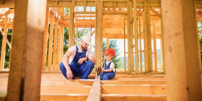 Muž a malý chlapec v pracovním oděvu v interiéru rozestavěné dřevostavby 