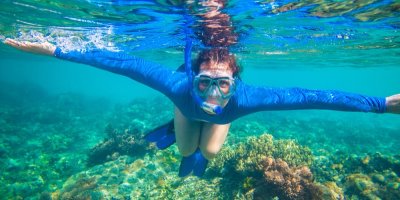 Žena v modrém triku šnorchluje v moři.