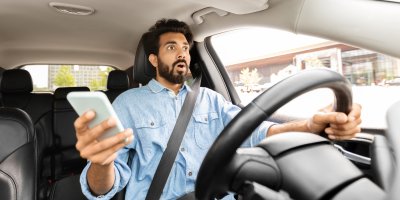 Muž se diví za volantem a drží v ruce telefon