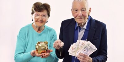 Seniorní pár drží v rukou zlatou pokladničku a české bankovky