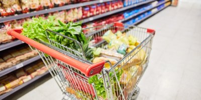 Nákupní vozík plný potravin stojí uprostřed uličky v obchodě