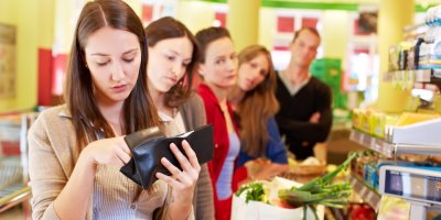 Žena u pokladny vybírá peníze z peněženky, za ní stojí dlouhá fronta rozladěných zákazníků