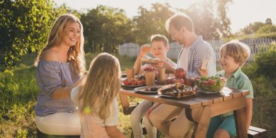 Pětičlenná veselá rodina snídá u dřevěného stolku na zahradě