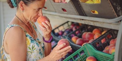 Žena drží v každé ruce broskvi a k jedné si voní