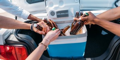 Skupinka lidí vytahuje lahve piva z chladicího boxu v autě