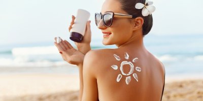 Žena v slunečních brýlích má na zádech slunce namalované opalovacím krémem, krém si dává na ruku