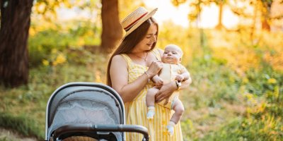 Žena drží v náručí malé dítě v přírodě během letního dne