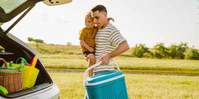 Otec nese dceru v náručí a ve druhé ruce má chladicí box