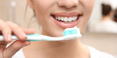 Usmívající se žena s dokonalým chrupem drží v ruce zubní kartáček se zubní pastou