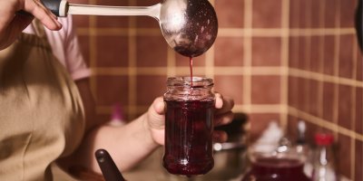 Člověk naběračkou nalévá marmeládu do sklenice