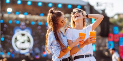 Dvě ženy se baví před koncertovým pódiem s kelímky v rukou.