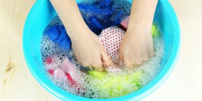 Dvě ruce perou ve škopku plavky