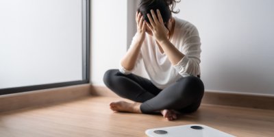 Žena sedí s rukama v dlaních před váhou