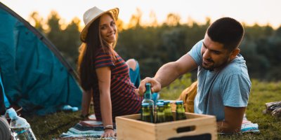 Mladý pár sedící u stanu s bedýnkou plnou piv