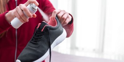 Žena stříká deodorant dovnitř sportovní boty.