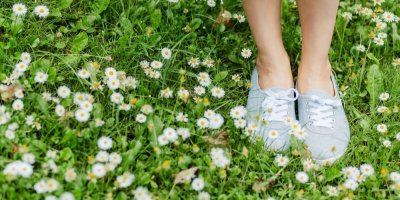 Nohy v lehkých šedých botách na trávníku mezi sedmikráskami