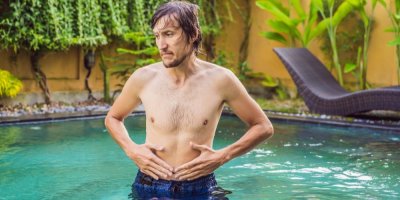 Muž stojící ve vodě se drží rukama za břicho