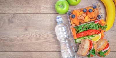 Sendviče, zelenina, ovoce a oříšky v sendvičovém boxu, vedle lahev s vodou